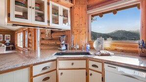 Eine Holzhütte mit einer Küche, einem großen Fenster, Holzschränken und einer Arbeitsplatte aus Granit.