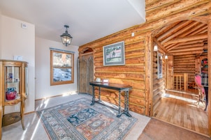 Interior de una cabaña de madera con un ventanal grande, una alfombra, una mesa y una silla.