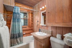 Une salle de bain rustique, avec une cabine en bois, une baignoire, un lavabo et des toilettes.