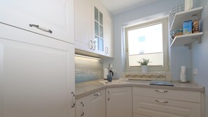 A kitchen with white cabinets, a window with a plant, and a shelf with items. - App. Hamelmann - with a small sea view (Sylt)
