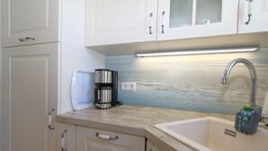 A kitchen with white cabinets, a coffee maker, a sink with a faucet, and a view of the sea through the window. - App. Hamelmann - with a small sea view (Sylt)