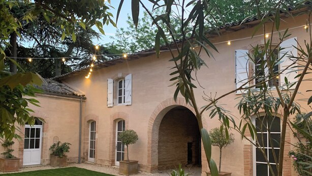 Un patio con camino de grava, plantas en macetas y luces colgantes.
