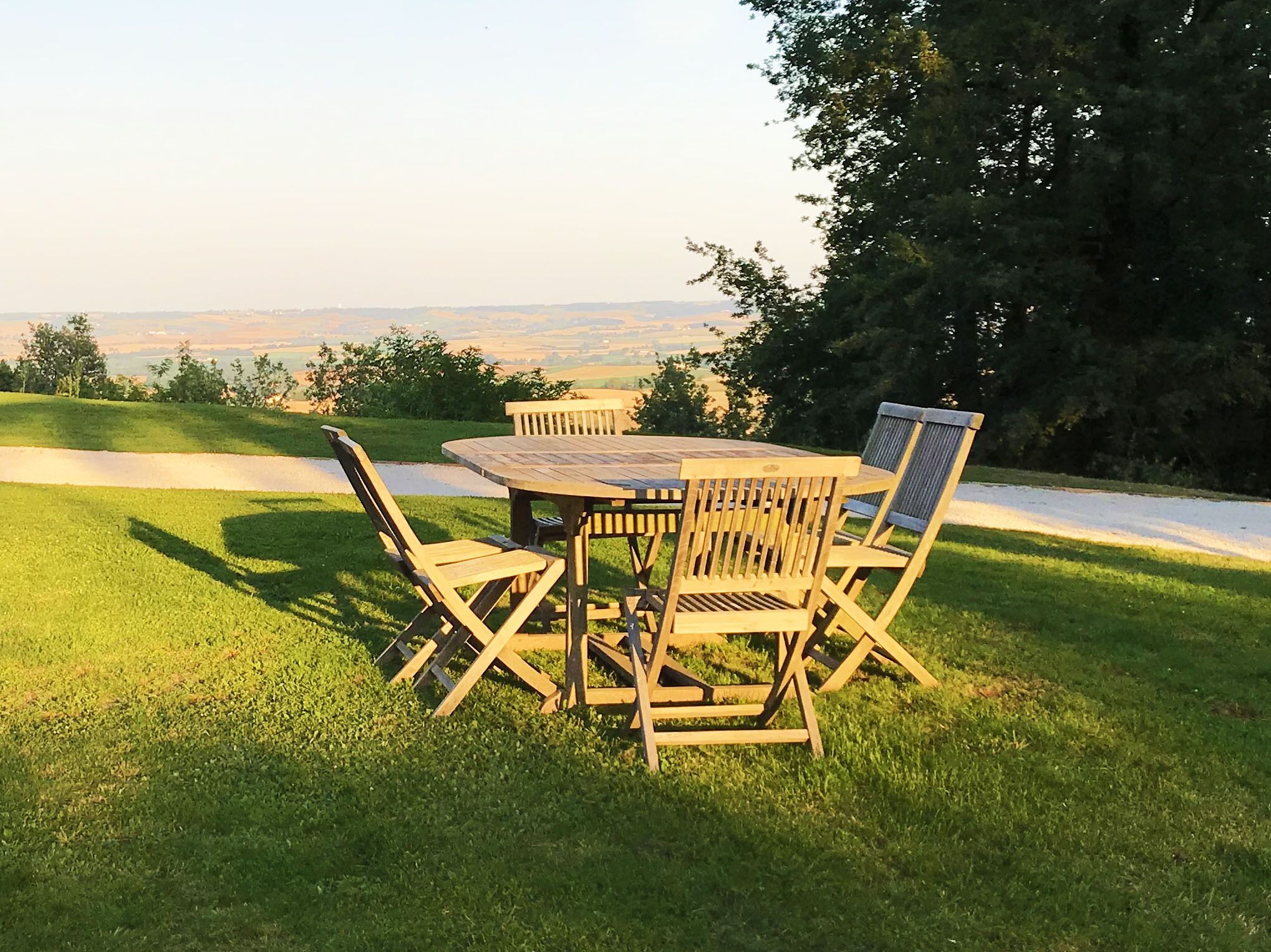 A wooden table and chairs set on a grassy lawn with a view of a distant landscape.