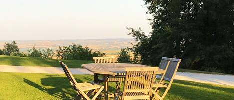 A wooden table and chairs set on a grassy lawn with a view of a distant landscape.
