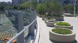 A rooftop terrace with concrete planters, a glass railing, and a view of high-rise buildings in the background. - Hangeul Guest House (Seoul)