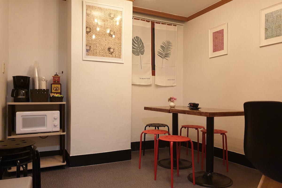 A small, cozy room with a wooden table and four red stools, a white microwave, and a shelf with kitchen items.