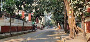 A tree-lined street with buildings on either side, including a visible sign on a tree trunk. - Daon Guest House Dhaka (Dhaka)