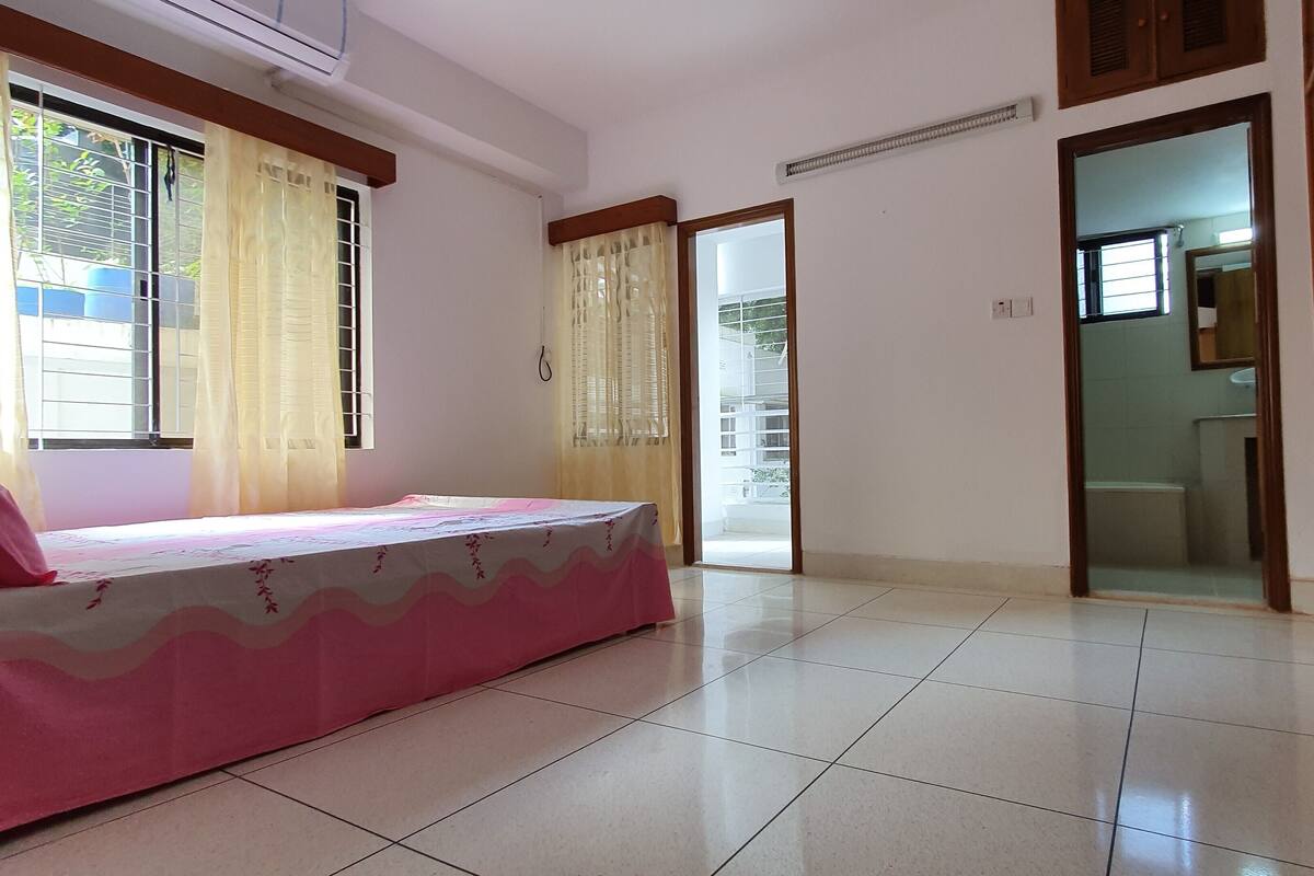 A room with a bed, a window with curtains, a door leading to a balcony, and a tiled floor.