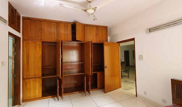 Una habitación amplia con un armario grande de madera, un ventilador de techo y suelo de baldosas.