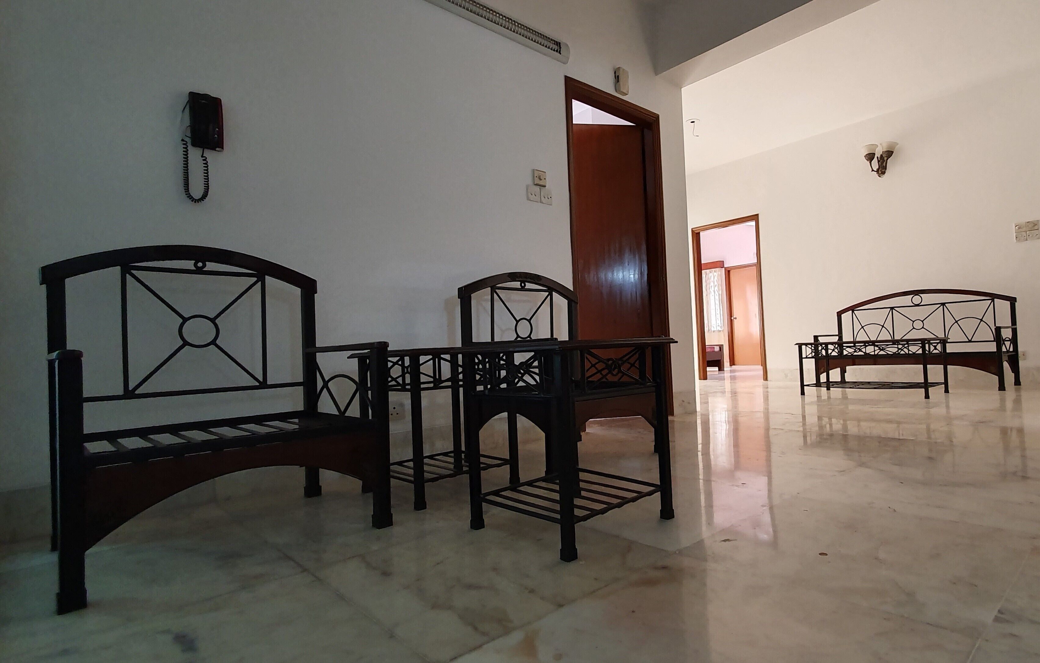 Una habitación con tres camas de madera, un teléfono en la pared y una puerta que da a otra estancia.