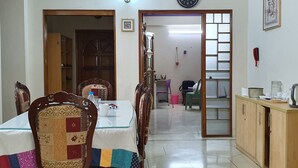 A dining area with a glass table, wooden chairs, and a clock on the wall. - Daon Guest House Dhaka (Dhaka)