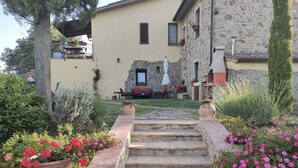 A stone staircase leading to a house with a stone facade, a small garden with pink flowers, and a patio area with outdoor furniture. - The casina of the NOT time downstairs (MONTEBUONO DI SORANO)