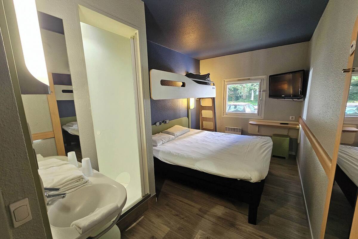 Une chambre à coucher de taille réduite, équipée d’un lit superposé, d’une table de chevet, d’un téléviseur et d’une fenêtre.