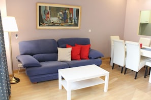 Una sala de estar con un sofá azul, una mesa de centro blanca y un cuadro en la pared.
