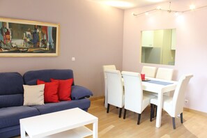 Ein Wohnzimmer mit einem blauen Sofa, roten Kissen, einem weißen Couchtisch und einem Essbereich mit weißen Stühlen und einem Tisch.