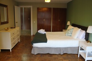 Een slaapkamer met een bed, een kaptafel, een nachtkastje, een lamp en een kledingkast.
