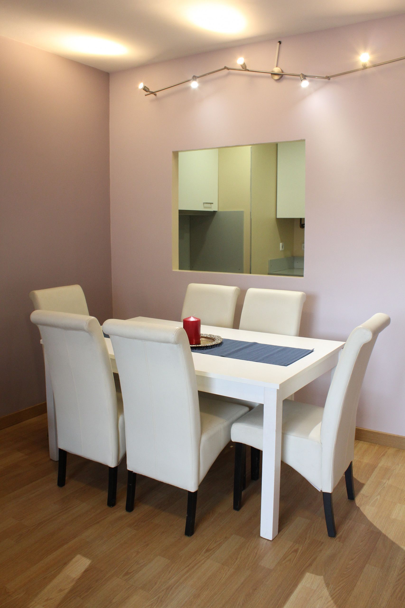 A dining area with a white table, four white chairs, a red cup, and a mirror on the wall.
