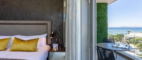 A hotel room with a bed, bedside table, lamp, and a view of the ocean through a balcony.