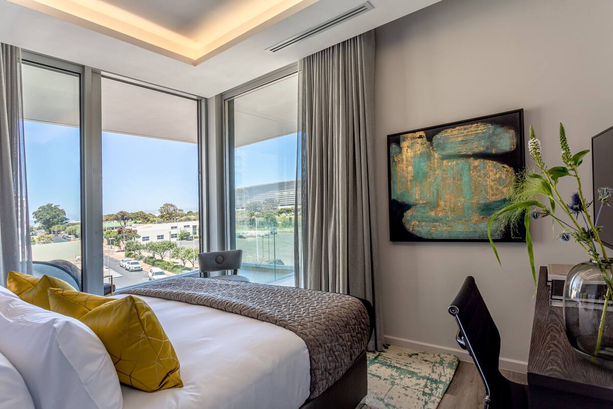 Une chambre d’hôtel avec un grand lit, un bureau et une vue sur la ville grâce à de grandes fenêtres.