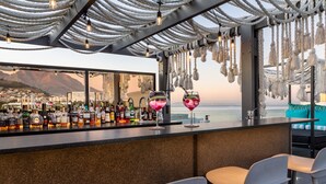 A bar with a view of the city and mountains, featuring a variety of bottles and glasses.