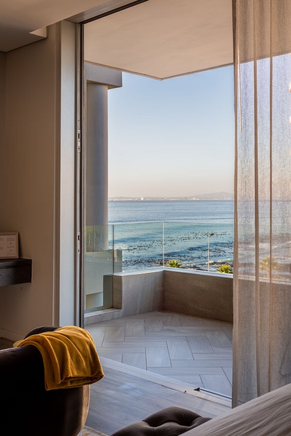 Un balcon avec vue sur la mer, une chaise recouverte d’un plaid jaune et un intérieur au design moderne.