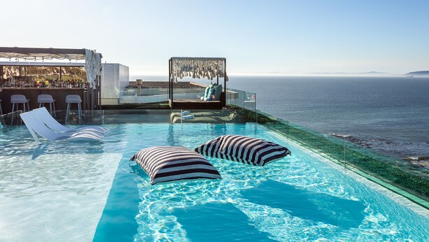 A pool area with lounge chairs and a bar overlooking the sea.