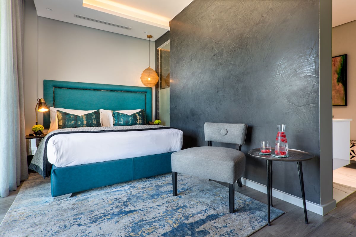 Une chambre d’hôtel moderne avec un grand lit, une chaise, une petite table avec des boissons et un mur à motifs.