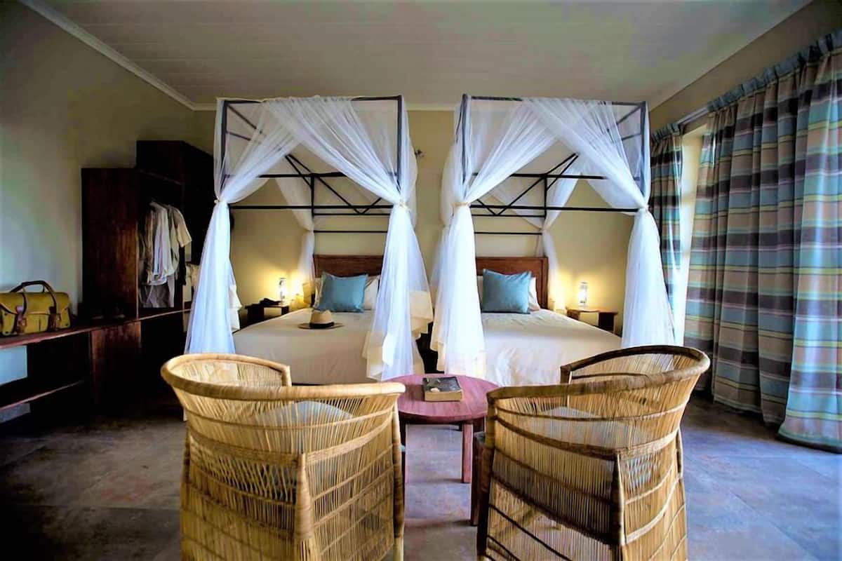 A double room with two beds, each with a canopy, a small table, and two wicker chairs.