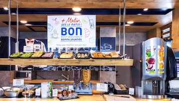 Un bufé de desayuno con diversas opciones de comida, una máquina de café y un cartel que anuncia un desayuno matutino.