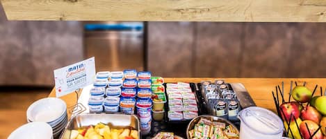 A buffet with various food items including fruits, cheeses, and packaged snacks.