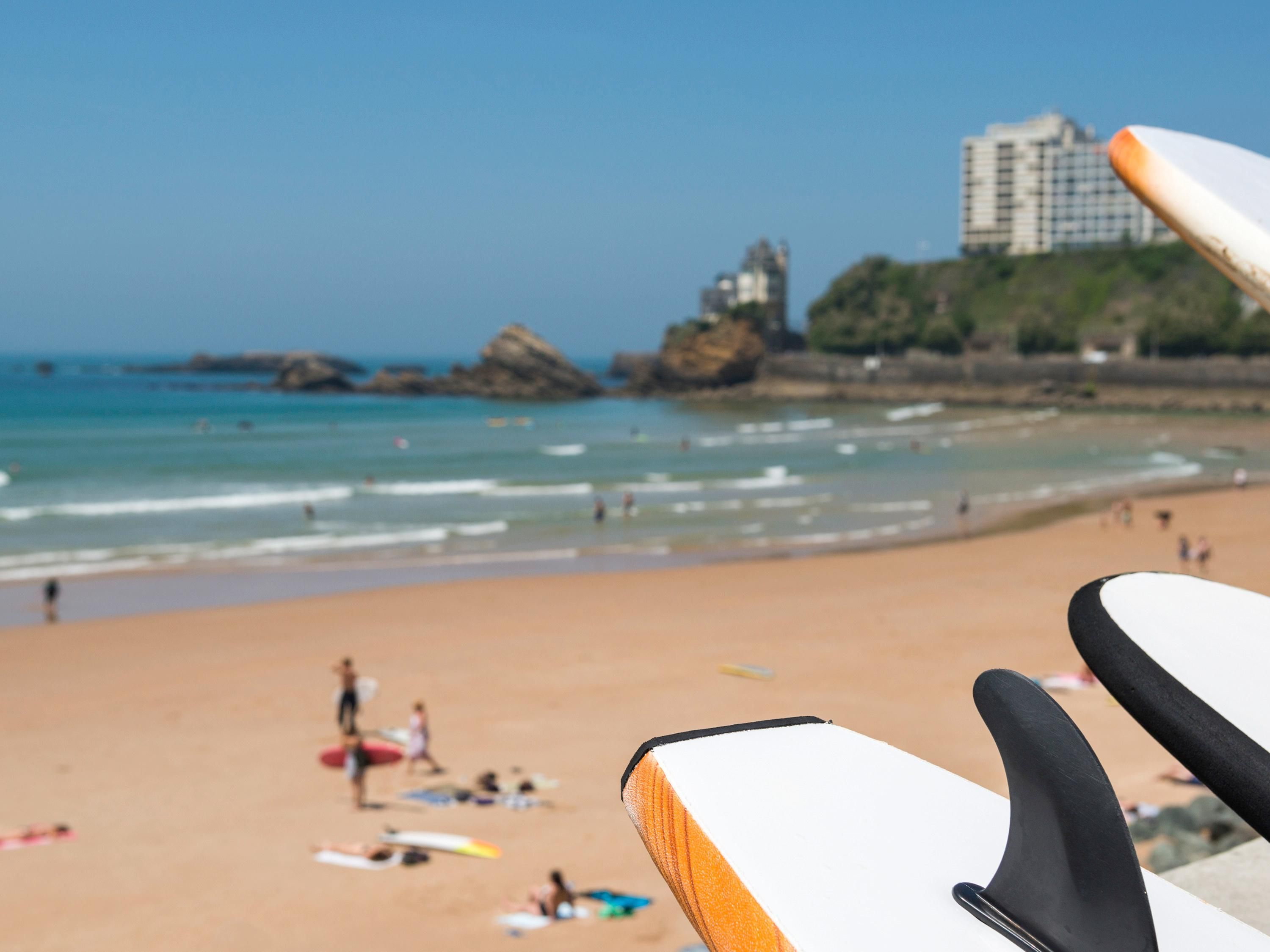 Una playa con tablas de surf, una orilla arenosa y edificios a la distancia.