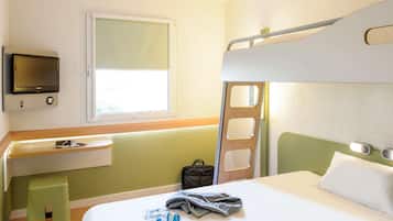 A hotel room with a bunk bed, a bedside table with a lamp, a TV mounted on the wall, and a window providing natural light.