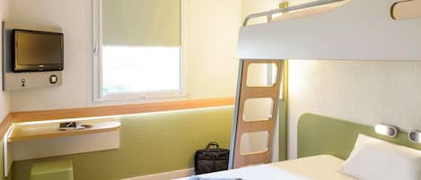 Habitación de hotel con una litera, una mesita de noche con lámpara, un televisor montado en la pared y una ventana que deja entrar luz natural.