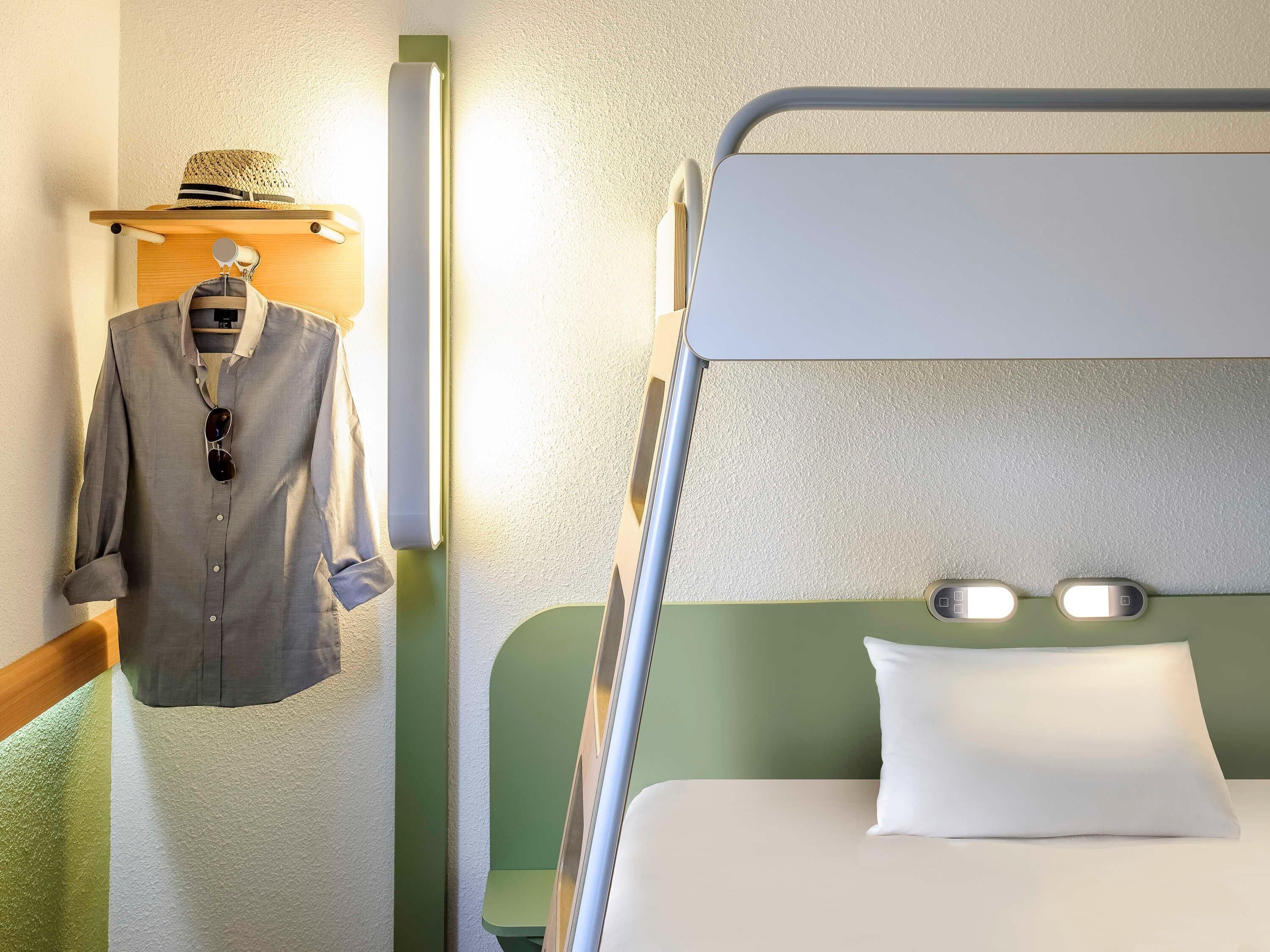 A bunk bed with a pillow and a hanging garment rack with a hat and a shirt.