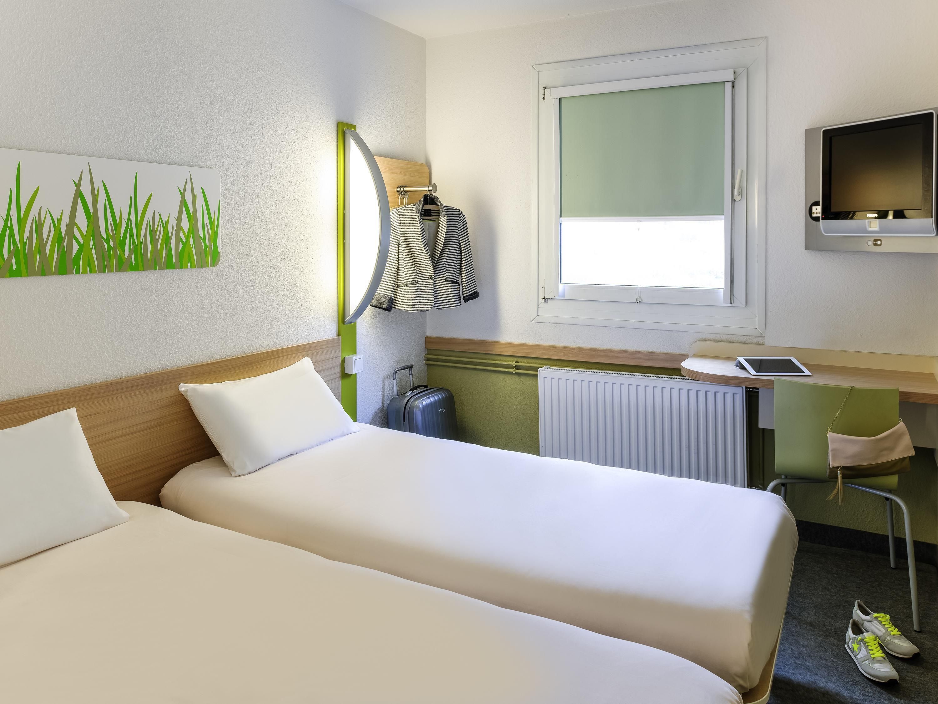 Habitación de hotel con dos camas, un escritorio con computadora, una ventana y un radiador.