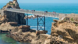 Un puente sobre terreno rocoso con una estatua en la cima, que conduce a la zona costera.