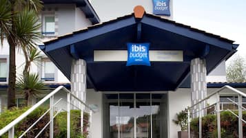 A modern hotel entrance with a sign indicating 'ibis budget hotels' and 'Biarritz-Anglet Airport' nearby.