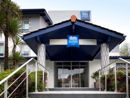 Una entrada de hotel moderna con un letrero que indica 'ibis budget hotels' y 'Aeropuerto de Biarritz-Anglet' cerca.