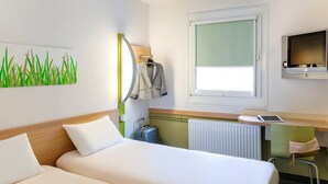 A hotel room with two beds, a desk with a computer, a TV, a window, and a radiator.