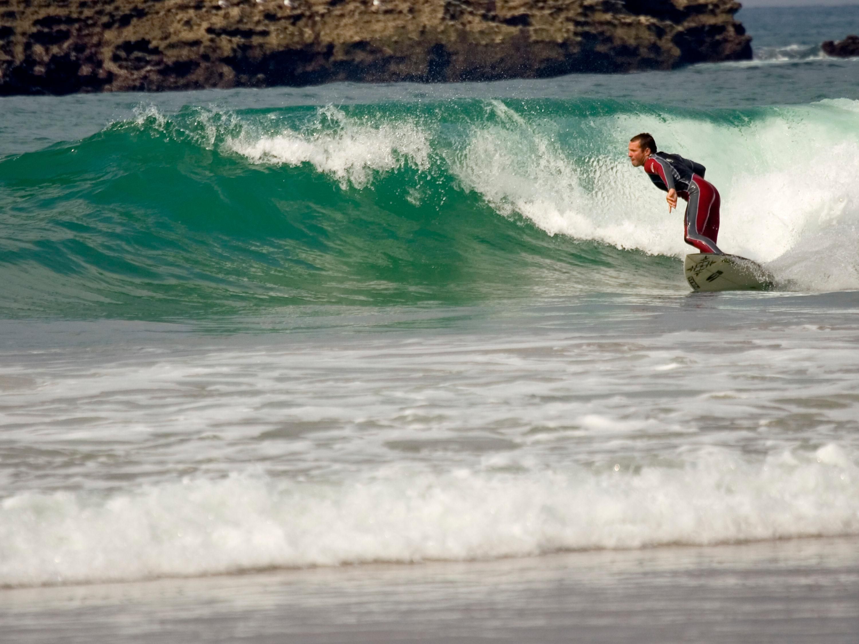 Un surfista cabalgando una ola en el océano, con una costa rocosa al fondo.