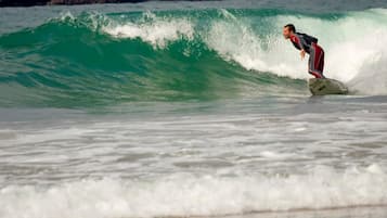 Un surfista cabalgando una ola en el océano, con una costa rocosa al fondo.