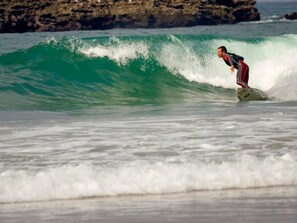 Un surfeur surfe sur une vague dans l’océan, avec une côte rocheuse en arrière-plan.