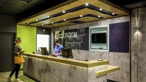 A reception desk with a modern design, featuring a concrete and wood finish, a large window, and a digital display. - Ibis Budget Biarritz Anglet (Anglet)