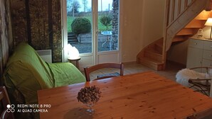 A cozy room with a wooden table, a green chair, and a staircase leading to an upper level. - Cottage "La Campagne" between sea and countryside (Heugueville-sur-Sienne)