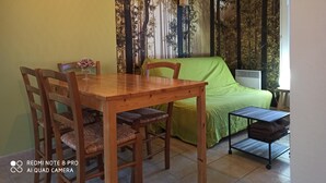 A dining area with a wooden table and chairs, a green sofa, and a small table with a lamp. - Cottage "La Campagne" between sea and countryside (Heugueville-sur-Sienne)