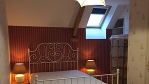 A bedroom with a sloped ceiling, a skylight, a white metal bed frame, two bedside lamps, and a wooden floor. - Cottage "La Campagne" between sea and countryside (Heugueville-sur-Sienne)