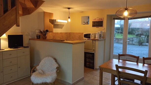 A modern kitchen with a wooden island, a dining area with a table and chairs, and a large window providing a view of the outdoors. - Cottage "La Campagne" between sea and countryside (Heugueville-sur-Sienne)