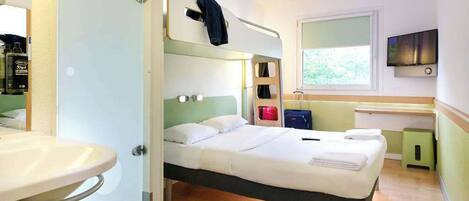 Habitación de hotel pequeña con una cama litera, una mesita de noche, un espejo, un televisor y una ventana con vistas a zonas verdes.