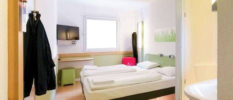 A hotel room with a bed, a TV, a window, a mirror, and a bathroom.