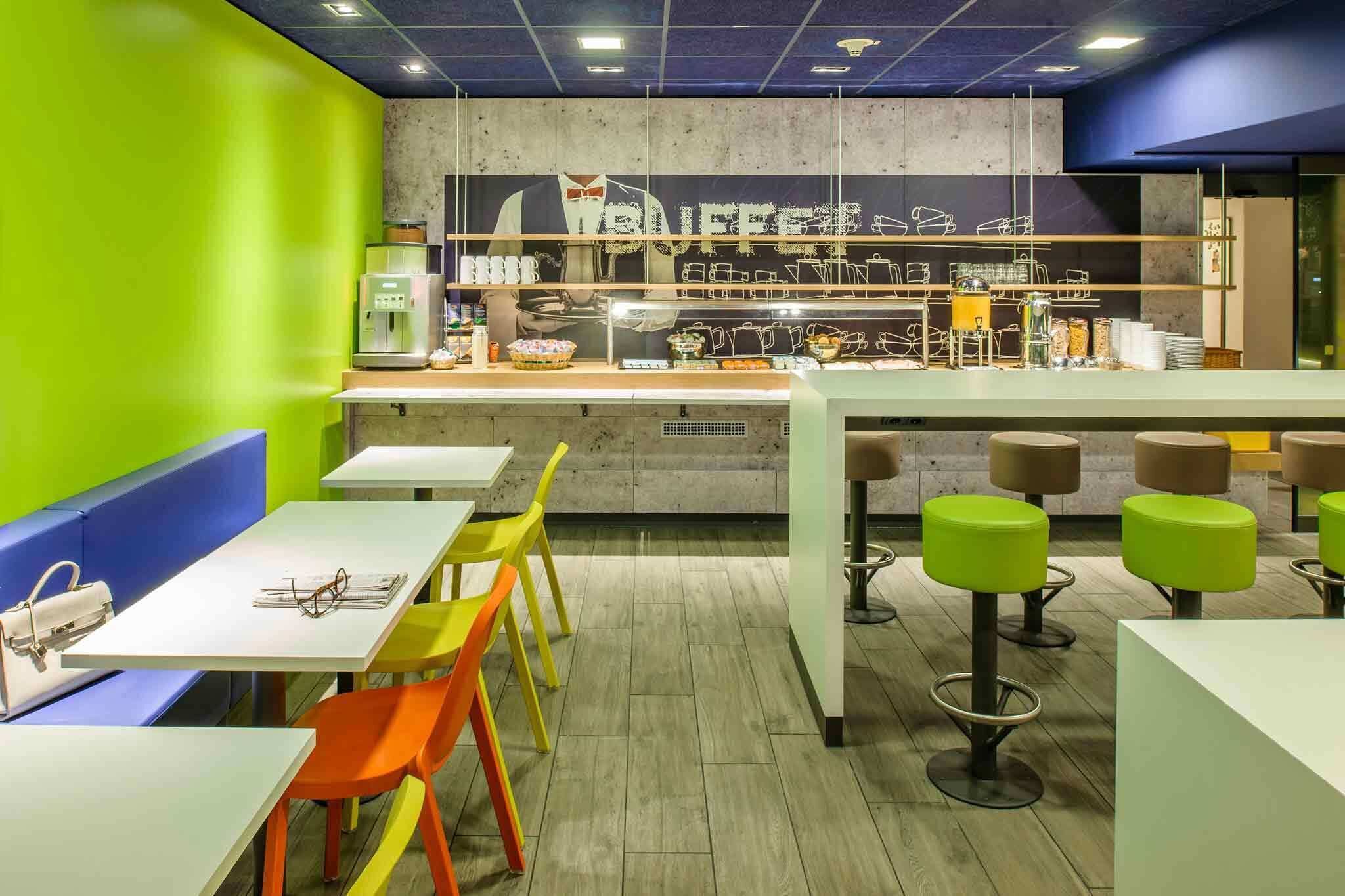 Een modern café met een bar, kleurrijke stoelen en een toonbank met verschillende producten.